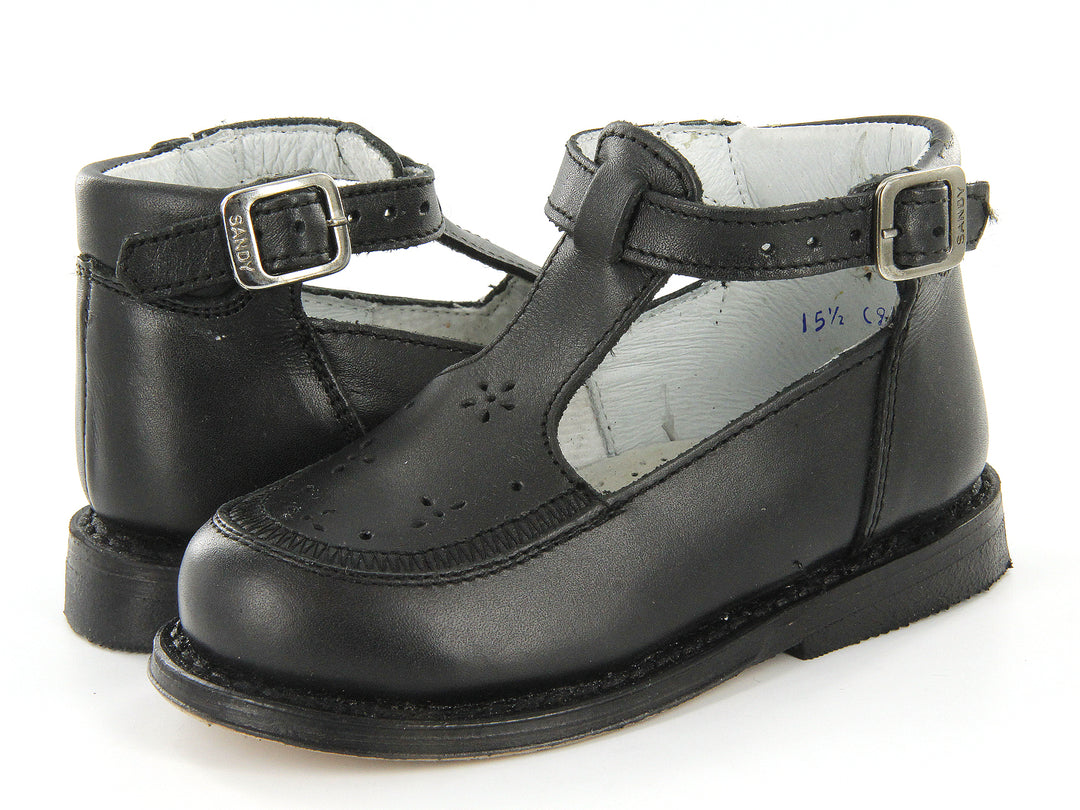 Par de zapatos negros clásicos para niño con correa y hebilla metálica sobre fondo blanco.