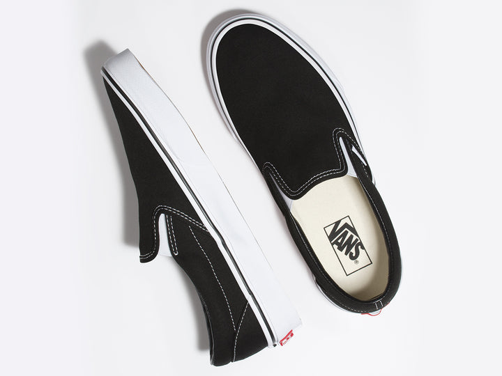 Tenis Vans Classic Slip-On color negro con suela blanca y diseño sin cordones.