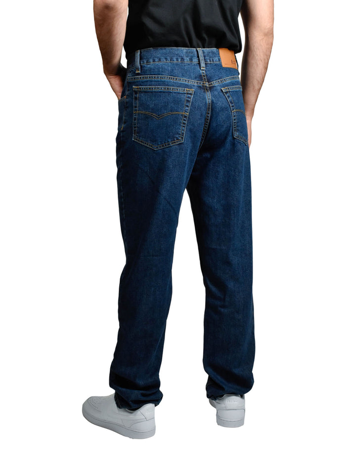 Hombre vistiendo pantalones jeans OGGI de color azul oscuro y tenis blancos sobre fondo blanco.