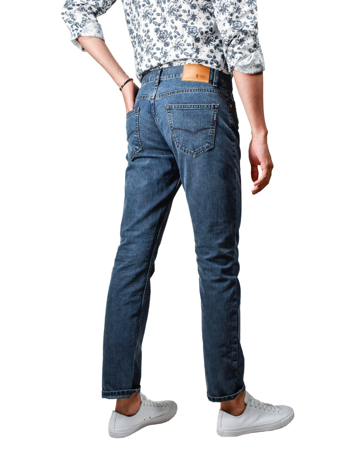 Hombre vistiendo jeans OGGI VAXTER color azul oscuro con tenis blancos.