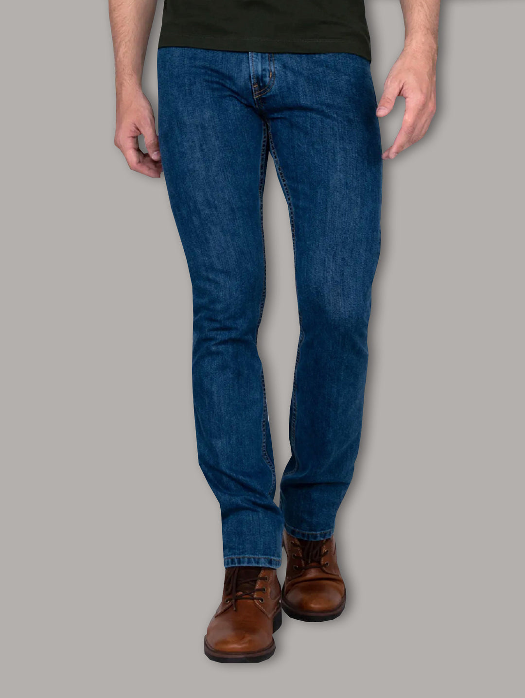 Hombre vistiendo jeans azul oscuro OGGI y botas color café sobre fondo gris.