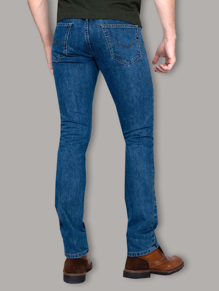 Hombre vistiendo jeans azul oscuro OGGI y botas color café sobre fondo gris.