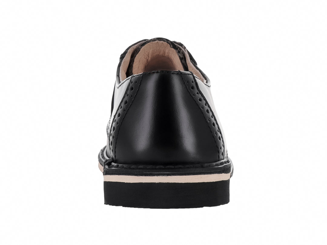 Zapato formal negro de cuero para niño con detalles perforados y suela blanca.