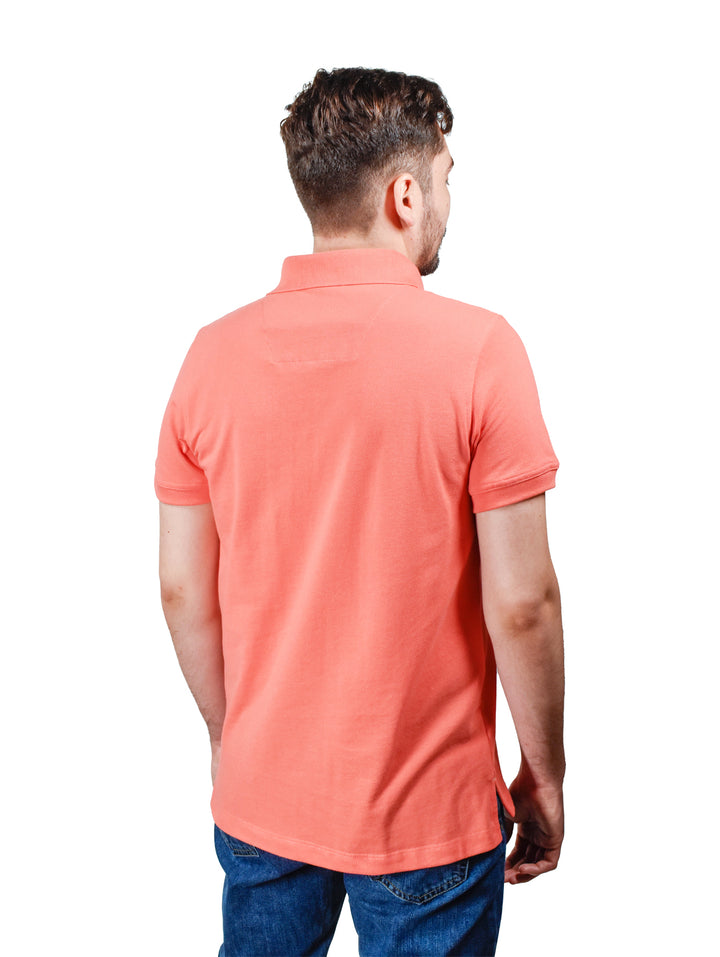 Hombre vistiendo una playera polo color coral de manga corta con cuello.