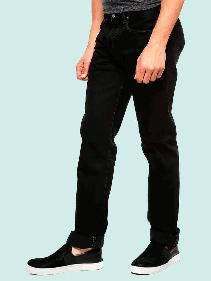 Hombre vistiendo pantalones jeans Levi's 501 color negro y zapatos negros con suela blanca.