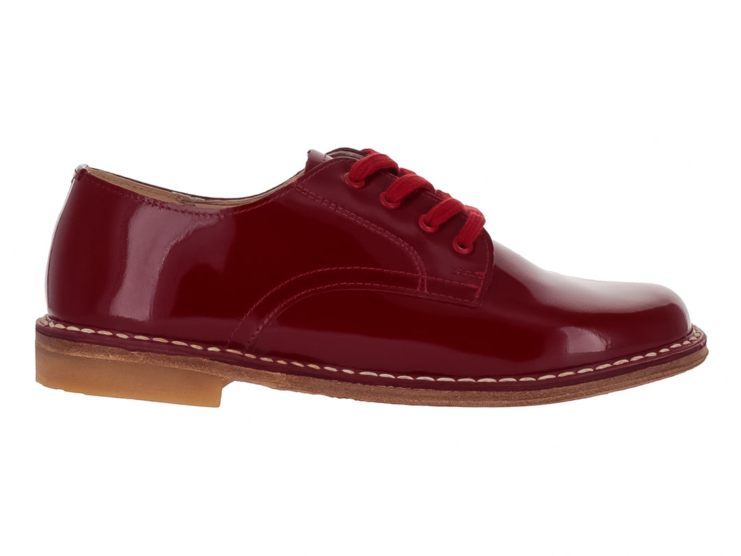 Zapato infantil de charol color rojo brillante con agujetas y costuras blancas en la suela.