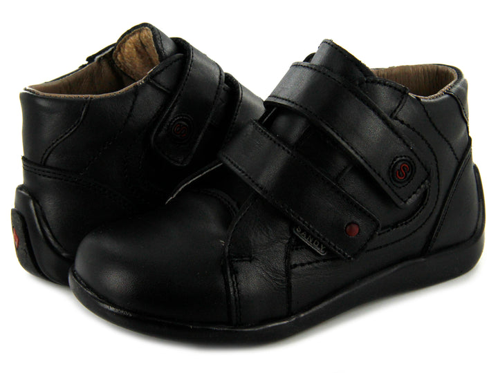 Par de zapatos negros para niño con cierre de doble correa de velcro y suela negra.