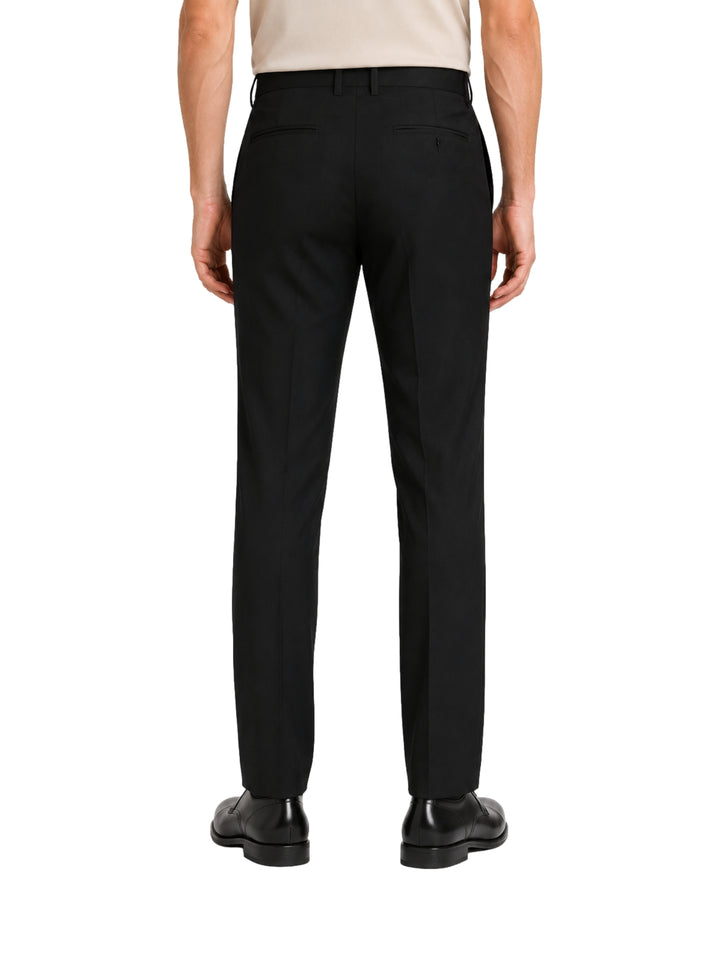 Hombre vistiendo un pantalón formal de color negro y zapatos negros sobre fondo blanco.