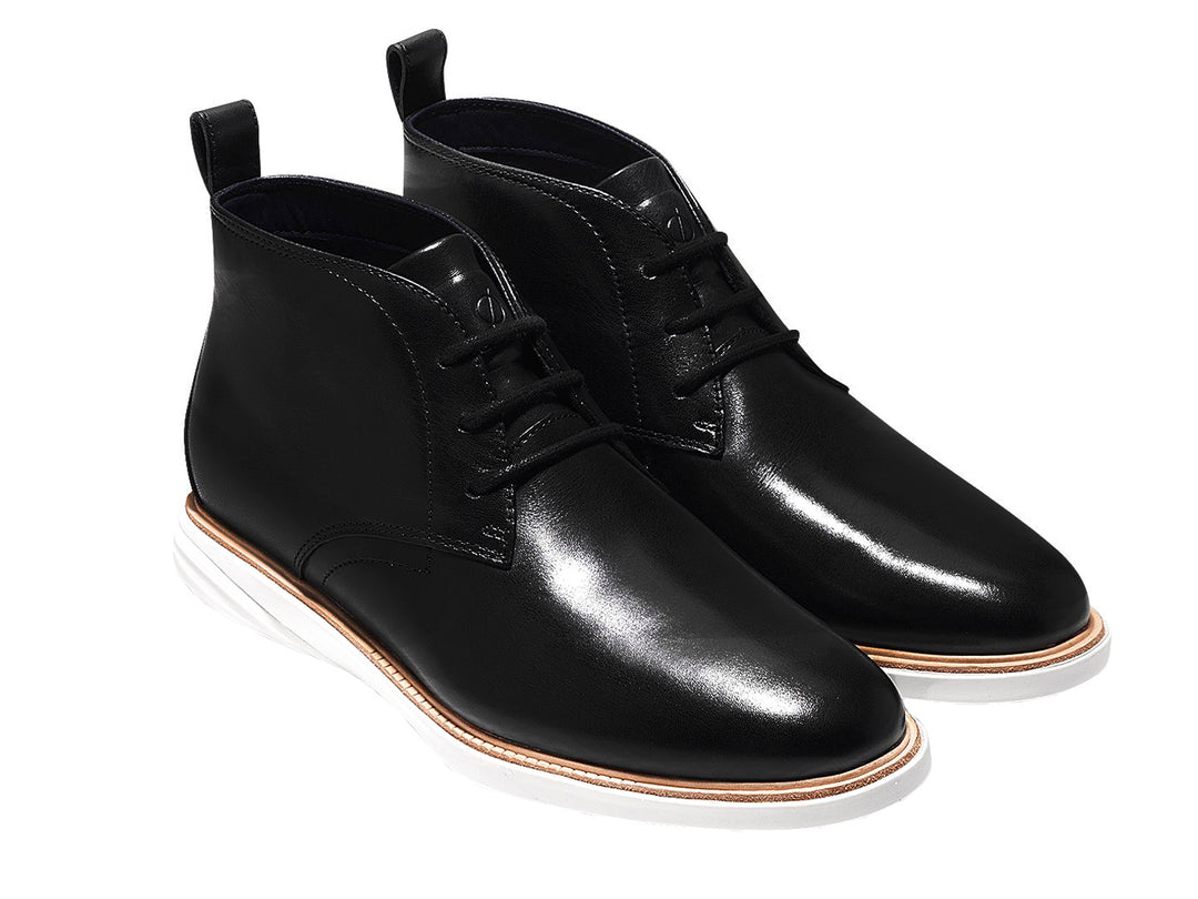 Par de botas chukka de cuero negro con suela blanca y cordones.