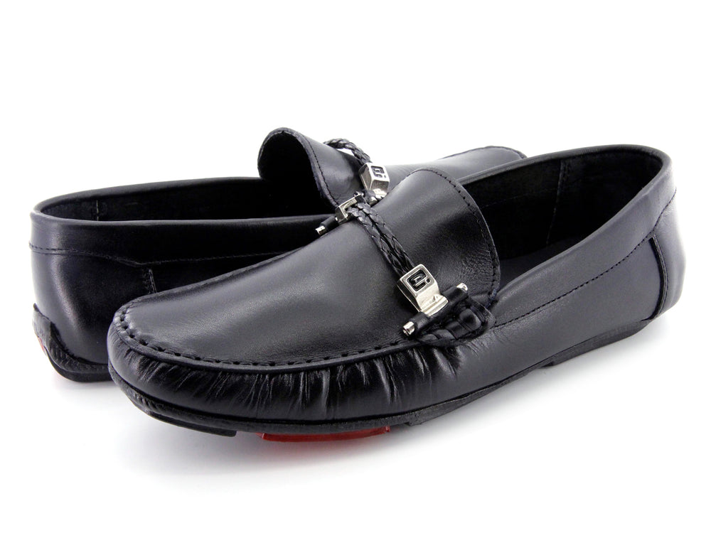 Zapato tipo mocasín de cuero negro con detalle de hebilla metálica y suela roja.