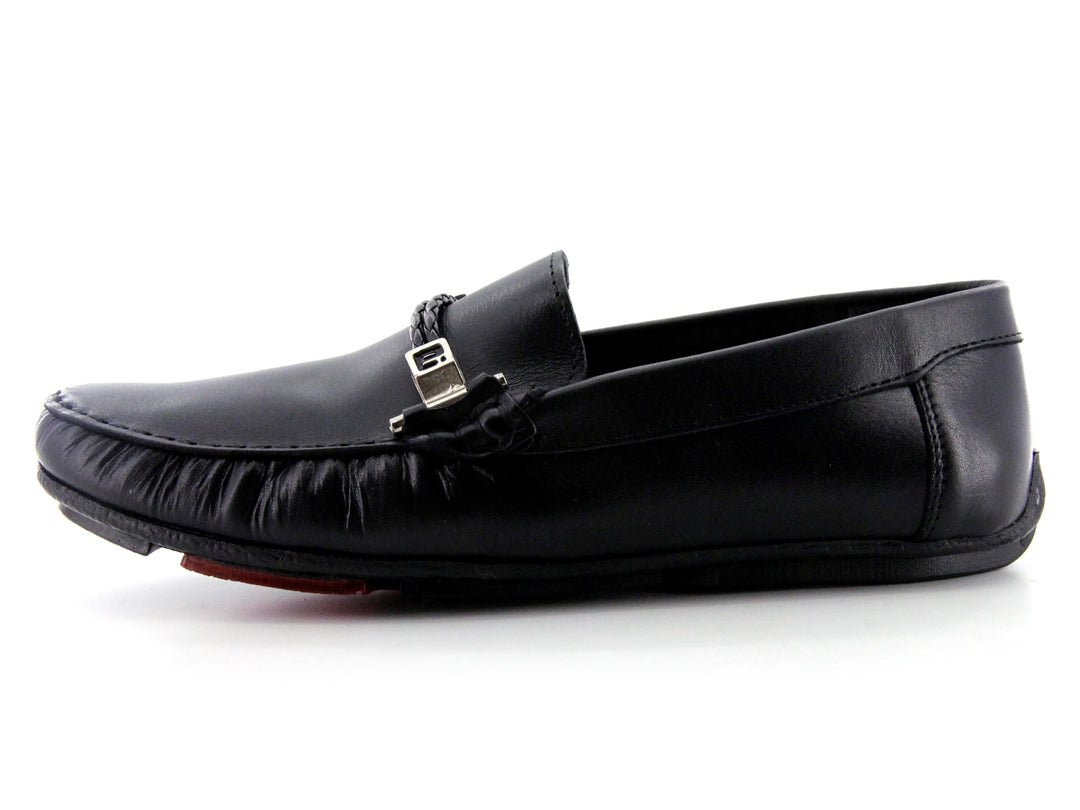 Zapato tipo mocasín de cuero negro con detalle de hebilla metálica y suela roja.