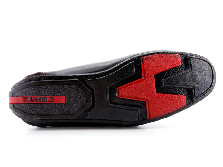 Zapato tipo mocasín de cuero negro con detalle de hebilla metálica y suela roja.