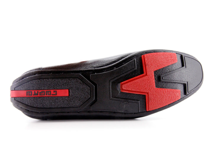 Zapato tipo mocasín de cuero negro con textura rugosa y detalle en la suela color rojo.