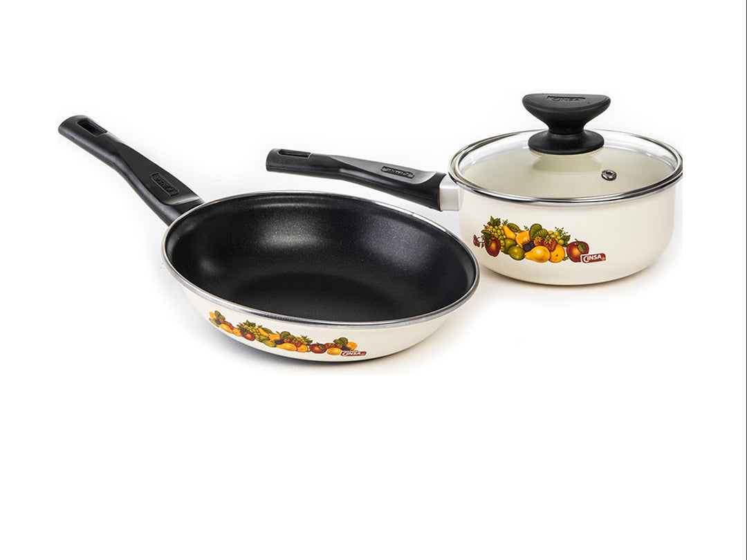 Batería de cocina blanca de 7 piezas con detalles de vegetales y mangos negros.