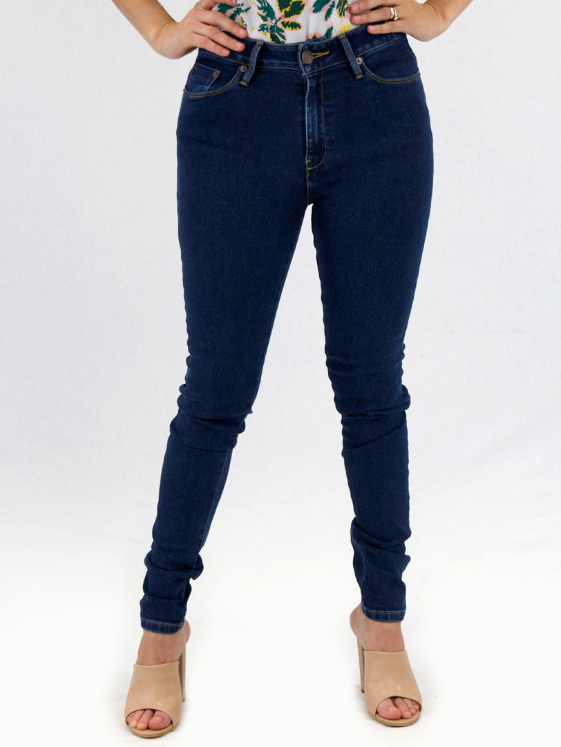 Mujer vistiendo jeans ajustados color azul oscuro con tacones beige sobre fondo blanco.