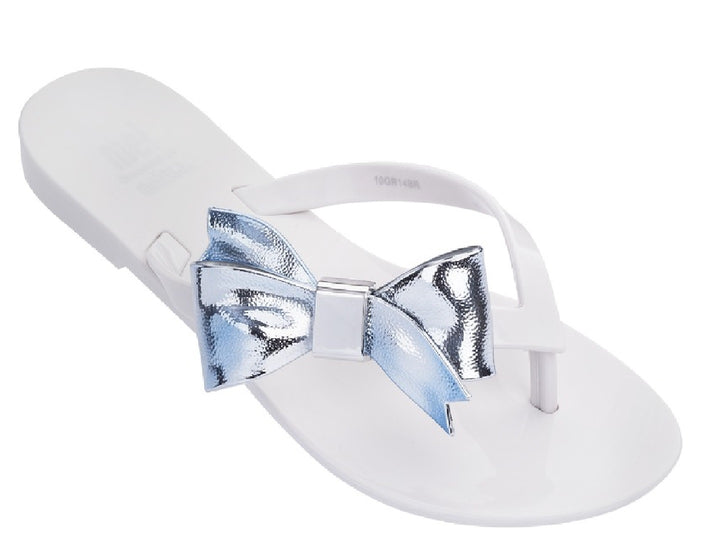 Sandalia blanca para niña con un moño plateado brillante en la parte superior.