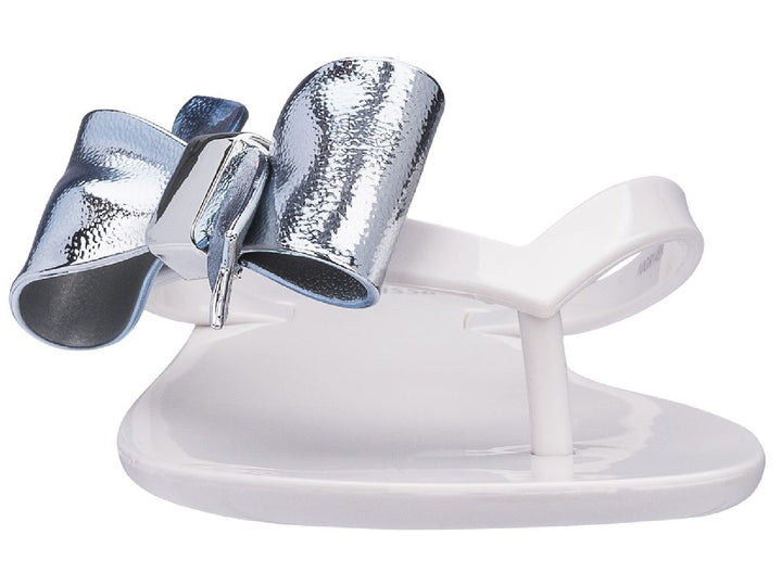 Sandalia blanca para niña con un moño plateado brillante en la parte superior.
