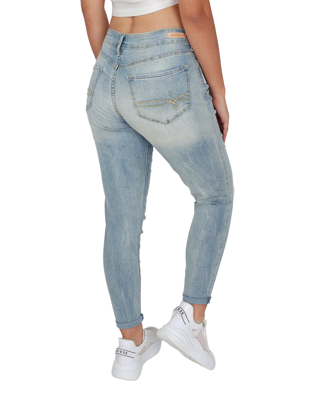 Mujer vistiendo pantalones jeans ajustados de color azul claro deslavado y tenis blancos.