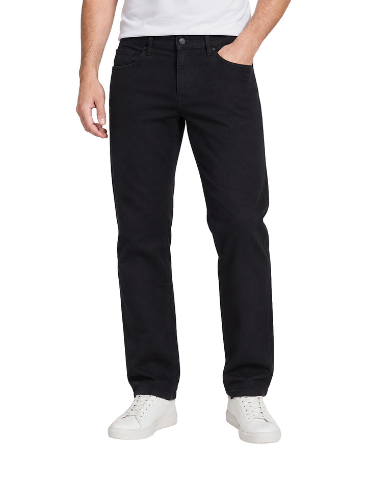 Hombre vistiendo jeans plus size de color negro, corte recto, combinados con camiseta blanca y tenis blancos.