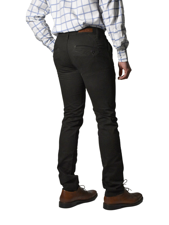 Hombre vistiendo un pantalón negro de corte recto con zapatos cafés y camisa a cuadros.