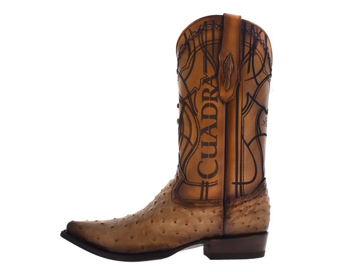 Par de botas vaqueras de cuero color taupe con bordados decorativos y textura granulada en la punta.