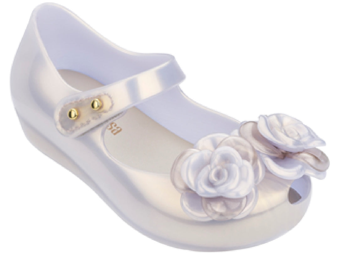 Sandalia transparente para niña con adornos de flores blancas y correa con remaches dorados.