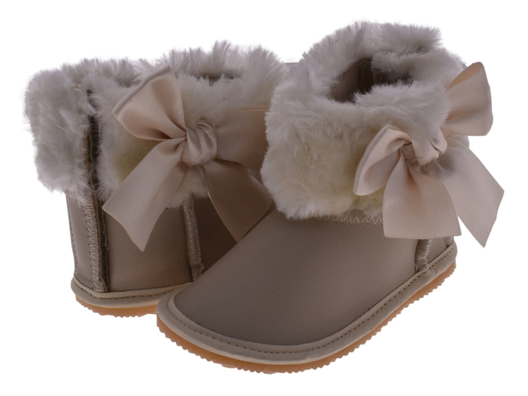 Par de botas color oro para bebé con detalles de moño y borde de peluche blanco.