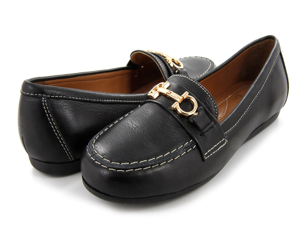 Par de mocasines de cuero negro con herraje dorado frontal y costuras blancas contrastantes.