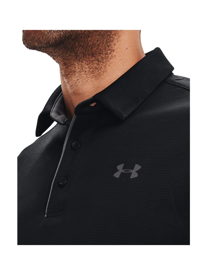 Hombre vistiendo playera polo deportiva Under Armour de color negro con detalles en gris.
