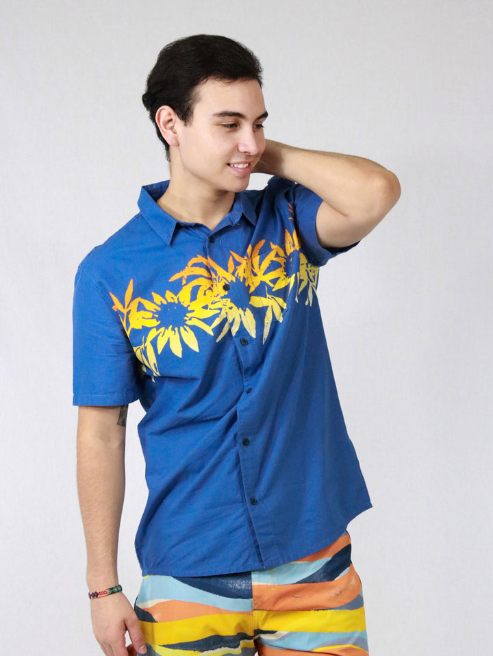 Hombre vistiendo camisa azul de manga corta con estampado floral amarillo en el pecho.
