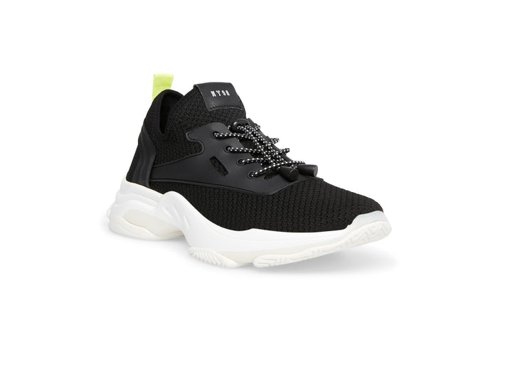 Tenis Steve Madden Isles Flyknit en color negro con suela blanca robusta y detalle amarillo neón en el talón.