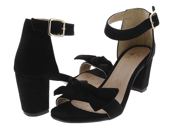 Sandalias negras de tacón grueso con moño frontal y correa al tobillo con hebilla dorada.