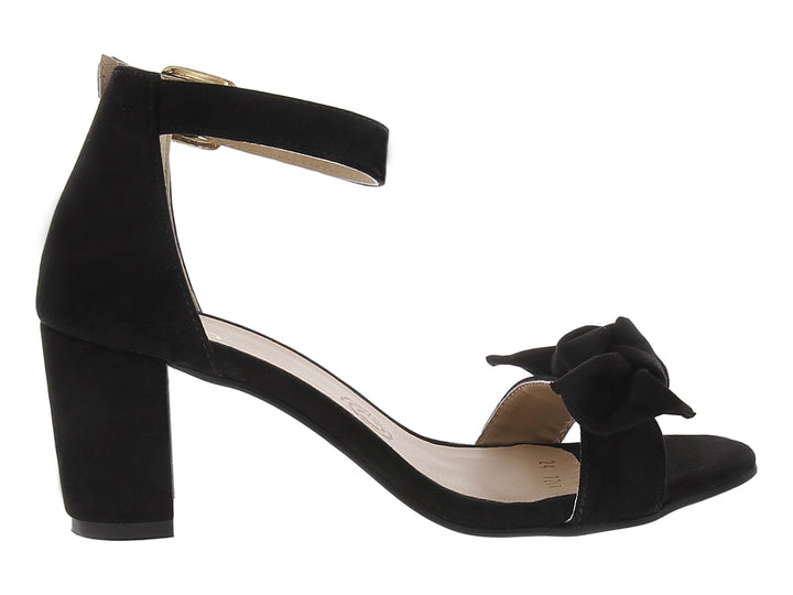 Sandalias negras de tacón grueso con moño frontal y correa al tobillo con hebilla dorada.