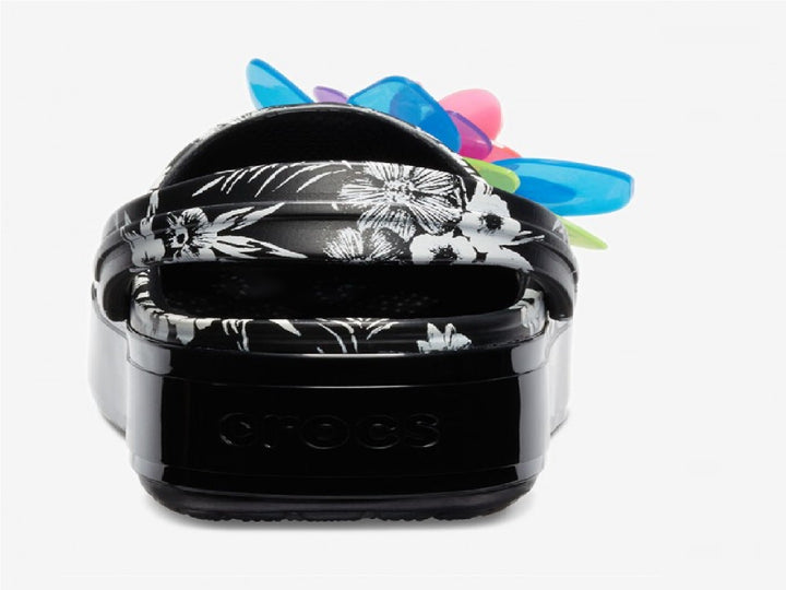 Zuecos Crocs negros con plataforma, estampado floral y una gran flor decorativa en colores neón.