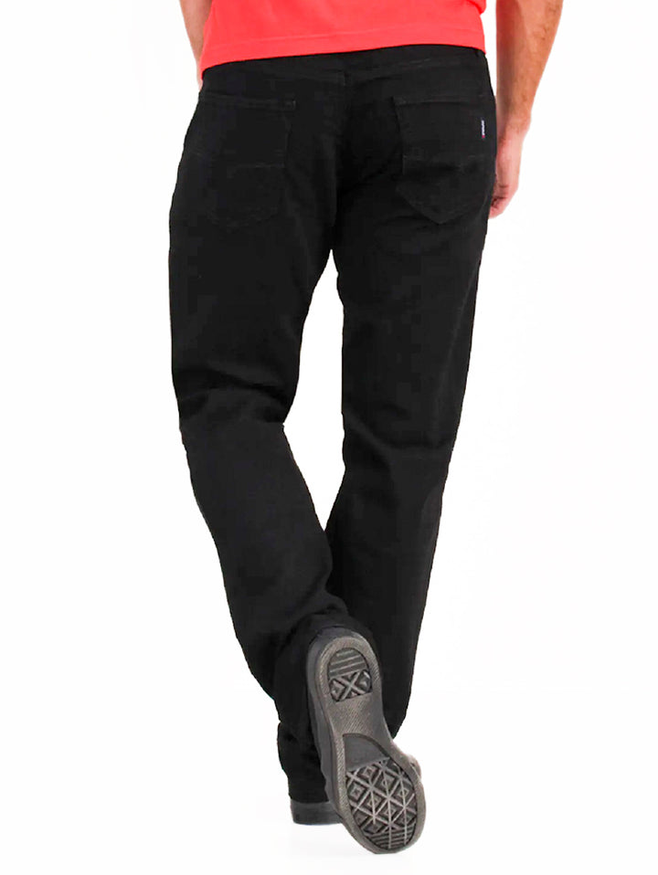 Hombre vistiendo pantalones jeans negros OGGI Vaxter, playera roja y tenis negros sobre fondo blanco.
