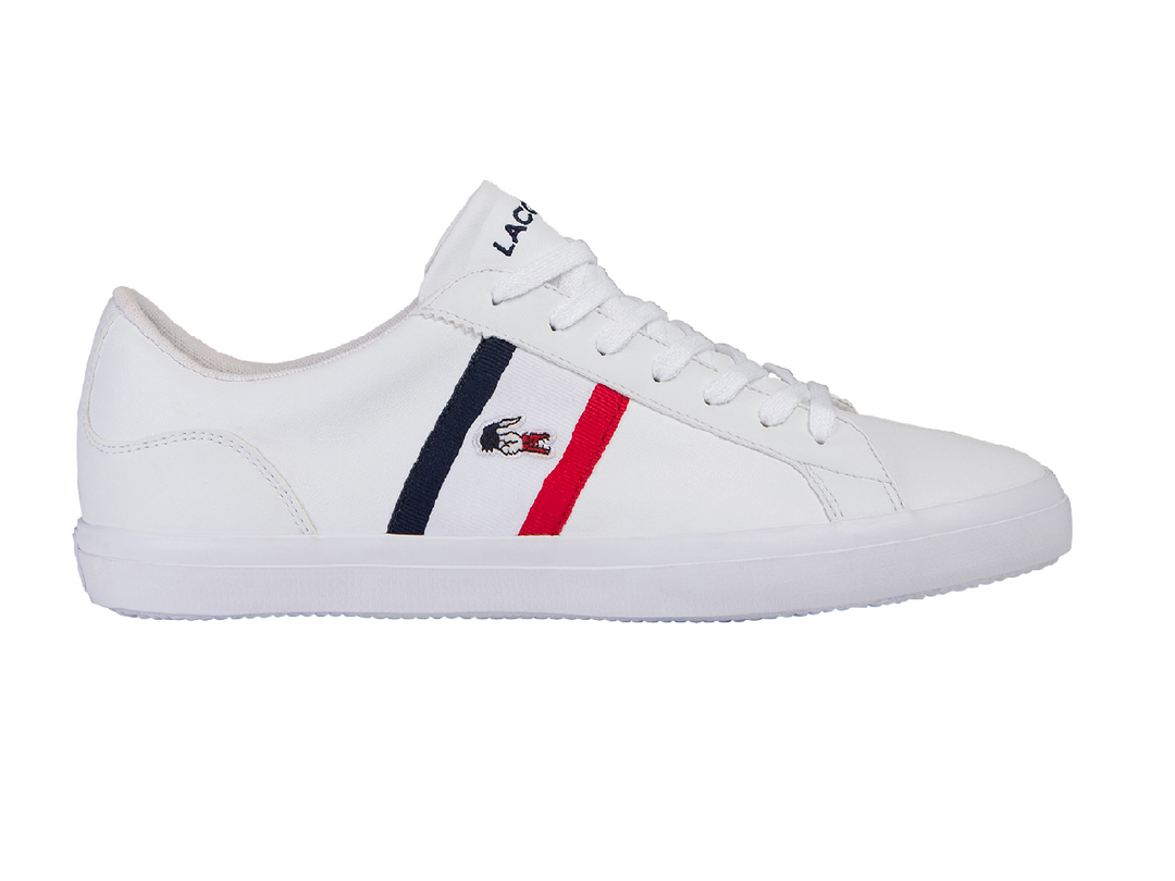 Tenis blancos Lacoste con rayas laterales en azul marino y rojo y suela blanca.
