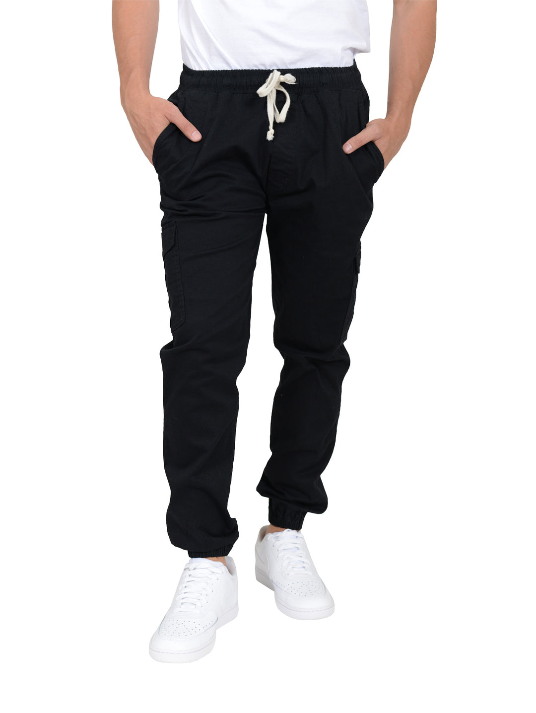 Hombre vistiendo joggers negros con cordones blancos y calzado blanco sobre fondo blanco.