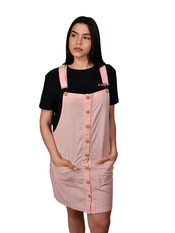 Mujer vistiendo un overol falda color rosa con botones frontales y tirantes sobre una camiseta negra.