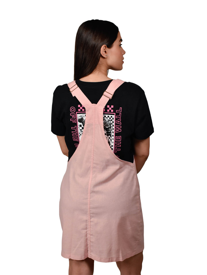 Mujer vistiendo un overol falda color rosa con botones frontales y tirantes sobre una camiseta negra.