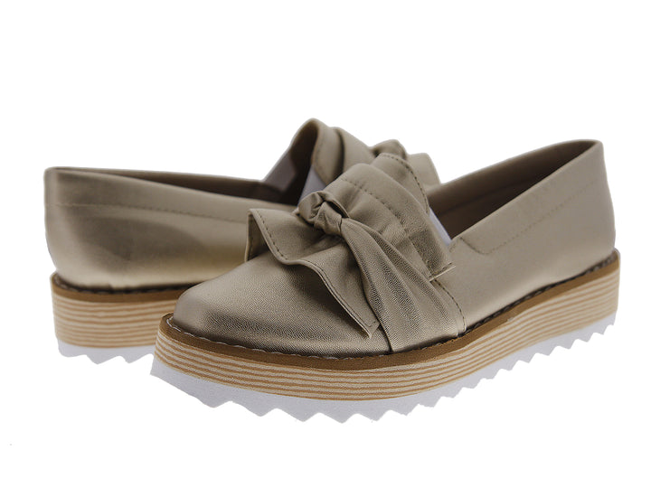 Zapatos mocasín color dorado metálico con moño frontal y suela de plataforma blanca y café.