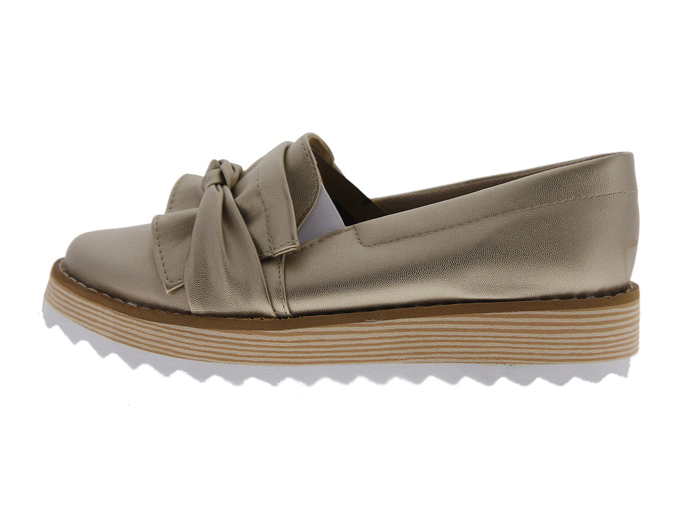 Zapatos mocasín color dorado metálico con moño frontal y suela de plataforma blanca y café.