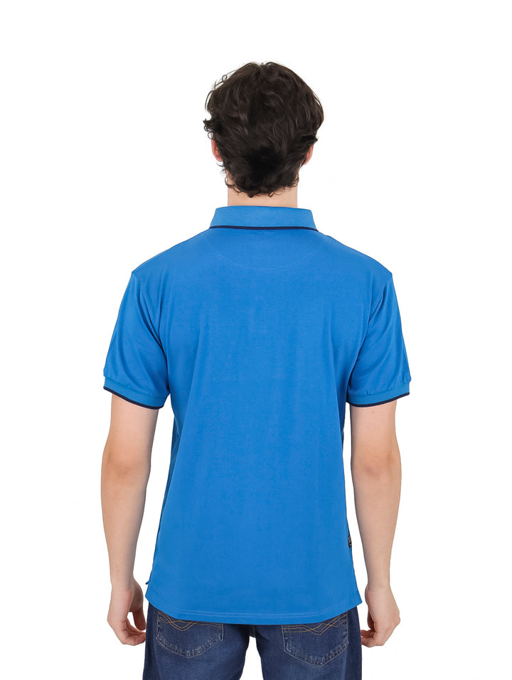 Hombre vistiendo una playera polo lisa de color azul con detalles en azul marino en los bordes de las mangas.