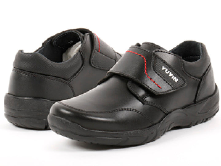 Par de zapatos negros para niño con cierre de velcro y detalles de costura roja.