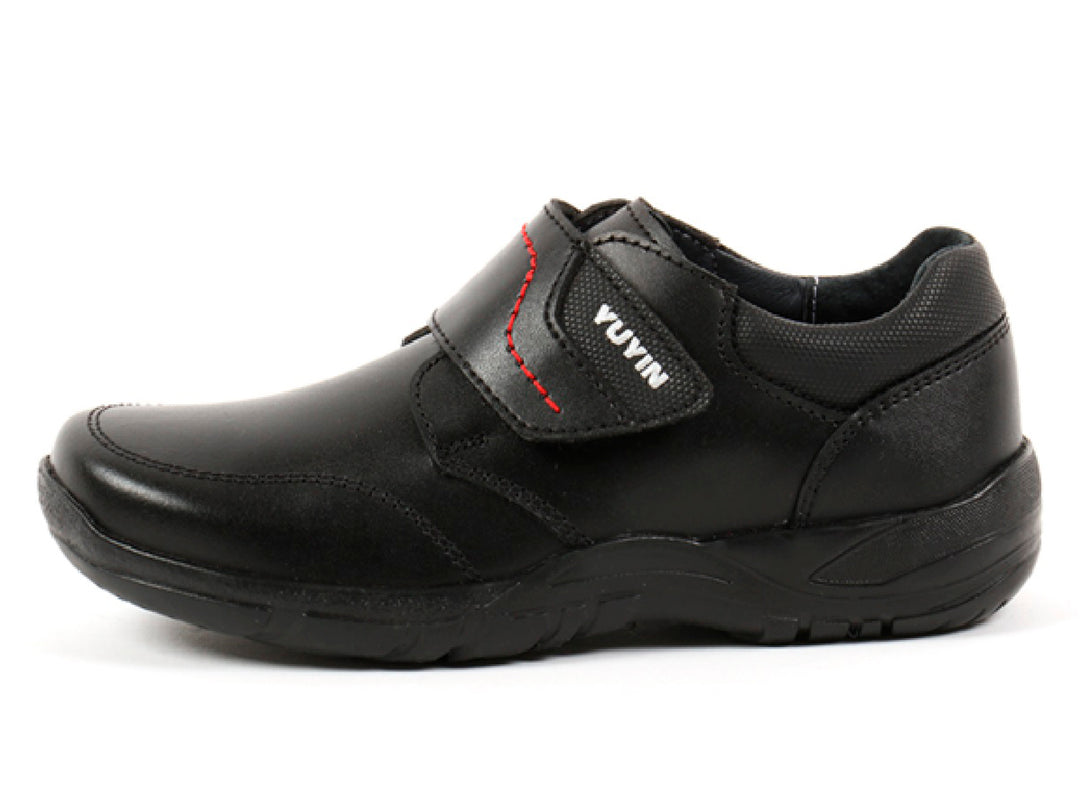 Par de zapatos negros para niño con cierre de velcro y detalles de costura roja.
