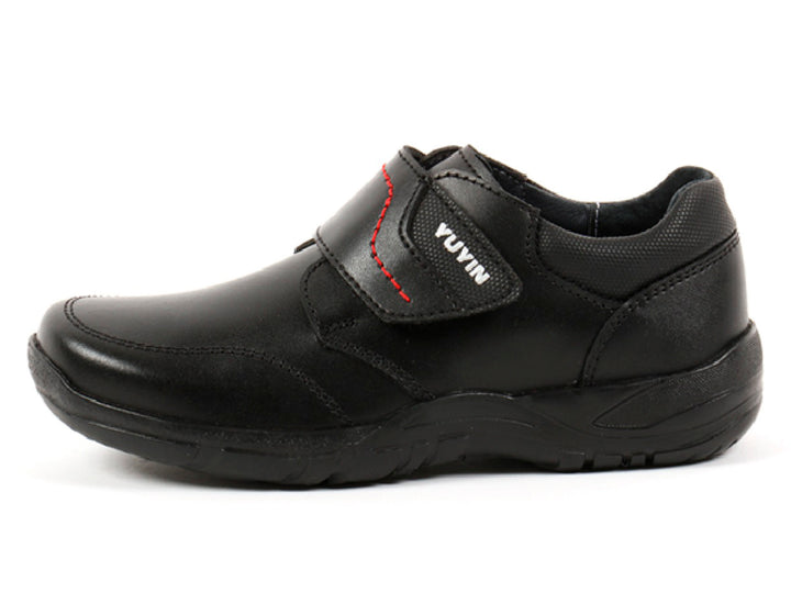Par de zapatos negros para niño con cierre de velcro y detalles de costura roja.