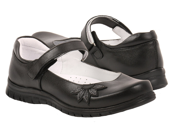 Par de zapatos negros para niña con correa y detalle floral en la punta.