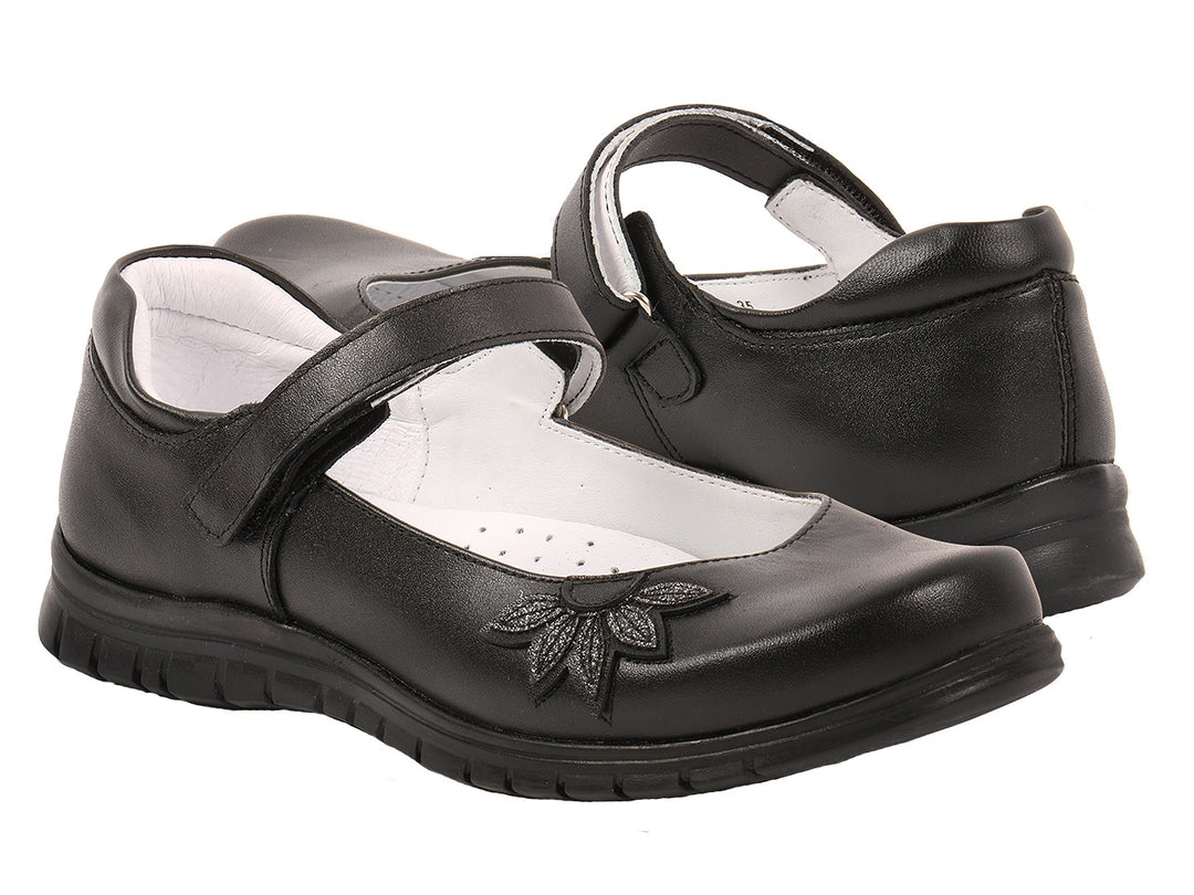 Zapatos negros para niña estilo Mary Jane con adorno floral en la punta y correa ajustable.