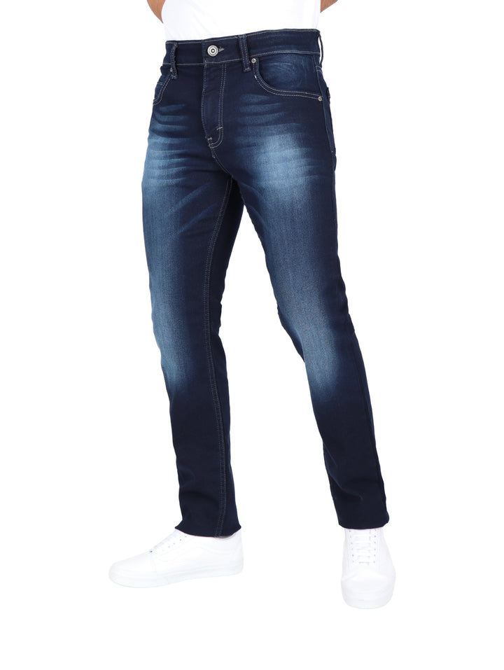 Jeans para hombre en color azul oscuro con efecto de lavado en los muslos y calzado blanco.