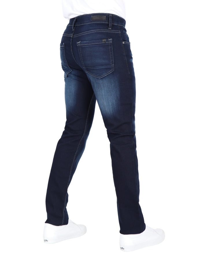 Jeans para hombre en color azul oscuro con efecto de lavado en los muslos y calzado blanco.