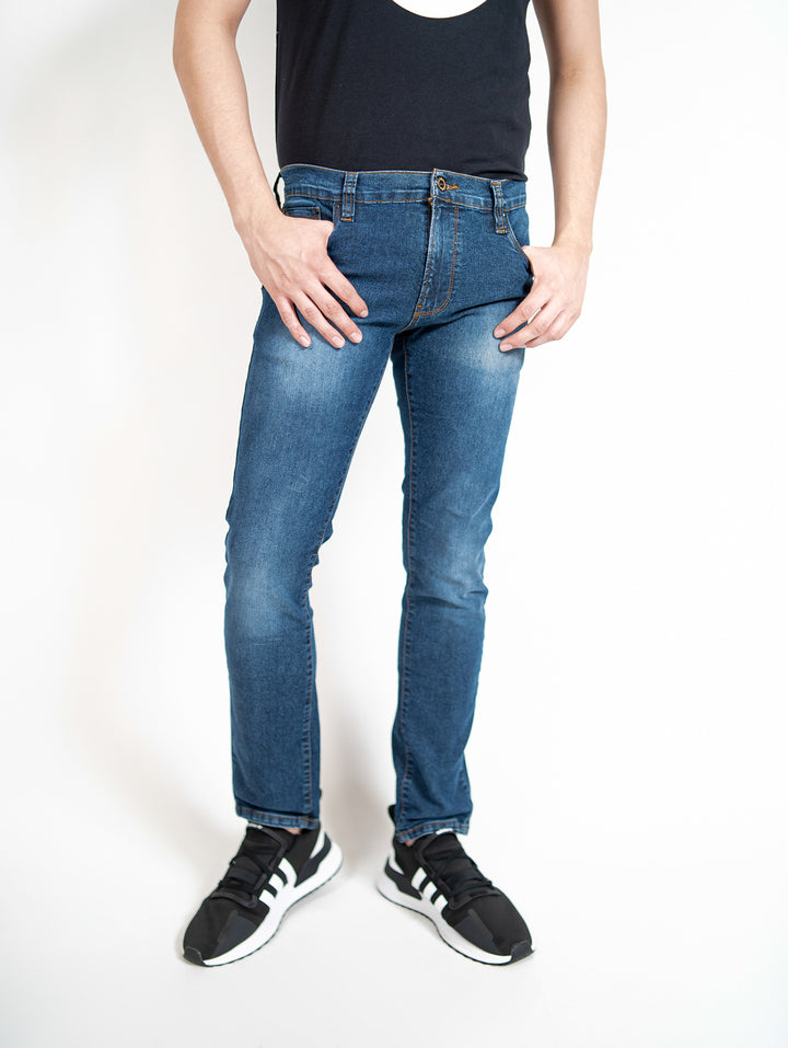 Hombre vistiendo pantalones de mezclilla azules ajustados y calzado deportivo negro sobre fondo blanco.